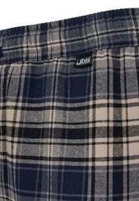 Pantalones cortos de pijama de cuadros en azul marino y beige que cuentan con una cinturilla elástica y una pequeña etiqueta negra con el logo "jbs". Tejido suave con un patrón de cuadros.