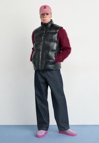 Svart pufferväst över en burgundy-färgad fluffig sweater, blå denimbyxor och ljuslila skor med rosa sulor, komplett med en rosa keps.