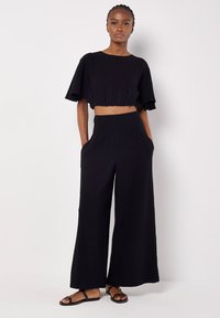 Completo coordinato nero composto da un top corto con maniche corte e pantaloni a gamba larga con vita arricciata e tasche laterali.