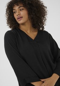 Black loose-fitting blouse with a v-neckline and three-quarter sleeves. Features soft, textured fabric with a subtle sheen.