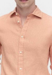 Perzikkleurig linnen overhemd met een button-down kraag, voorzien van een soepele textuur en witte knoppen langs de voorflap.