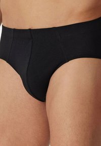 Zwarte katoenen slip met een gladde textuur, voorzien van een elastische tailleband en een gestroomlijnde vorm. Geen zichtbare patronen of accenten.