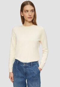 Kremowy sweter z długim rękawem i okrągłym dekoltem, o gładkiej fakturze i dopasowanej sylwetce, zestawiony z niebieskimi dżinsami z wysokim stanem.