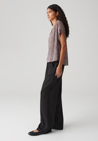Blouse à motifs floraux, à manches courtes, en rouge et blanc, associée à un pantalon noir ample et des ballerines noires.