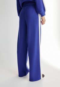 Pantaloni blue cu croi larg dintr-un material texturat, având o dungi laterale albe contrastante. Talie elastică și croi lejer.