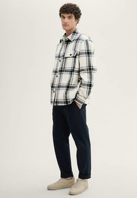 Kockás flaneling fehér, kék és fekete színekben, két elülső zsebbel. Sötét nadrággal és bézs tornacipővel párosítva.