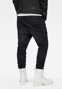 Černé denimové jogger kalhoty s tapered nohavicemi, vybavené několika kapsami, texturovaným povrchem a opotřebovanými detaily. Spárované s bílými bojovými botami.