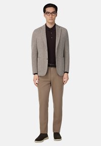 Grå texturerad kavaj över en mörk polo, kombinerad med beige chinos och mörka sneakers. Outfiten har en skräddarsydd passform och minimalistisk design.