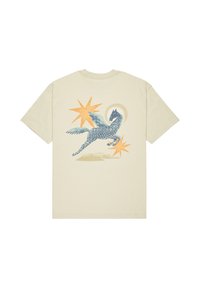 Crème-kleurig T-shirt met een grafiek van een blauw patroon van een gevleugeld wezen, versterkt door oranje sterren en een cirkelvormige achtergrond.
