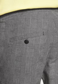 Czarno-białe spodnie w kratę z tylną kieszenią z patką i czarnym guzikiem. Tkanina ma teksturowany splot.