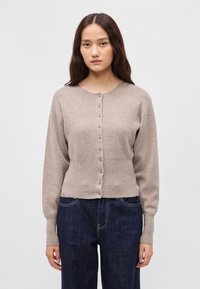 Κρεμ πλεκτό cardigan με μακριά μανίκια, κυκλικό λαιμό και μπροστινό κλείσιμο με κουμπιά. Ριμπέ υφή και εφαρμοστό σχέδιο στη μέση. Στυλιζαρισμένο πάνω από σκούρα τζιν.