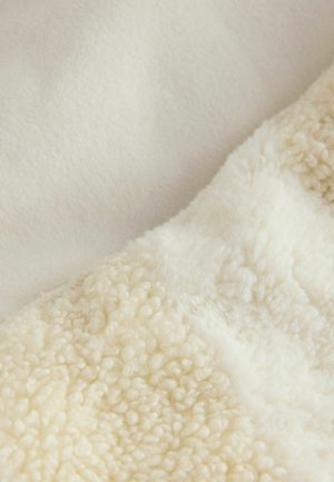 Coperta morbida in crema con due texture: una felpa liscia e un plush fluffy sherpa con fibre arrotondate e sollevate.