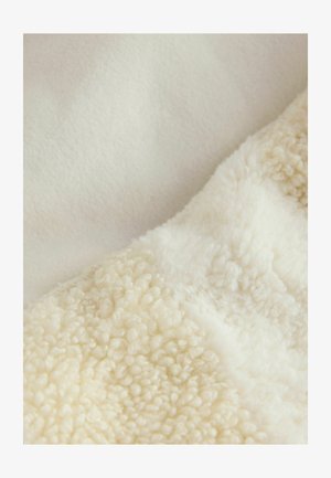 Puha krémszínű takaró, két textúrával: sima polár és bolyhos, pamutszerű sherpa kerek, kiemelkedő szálakkal.