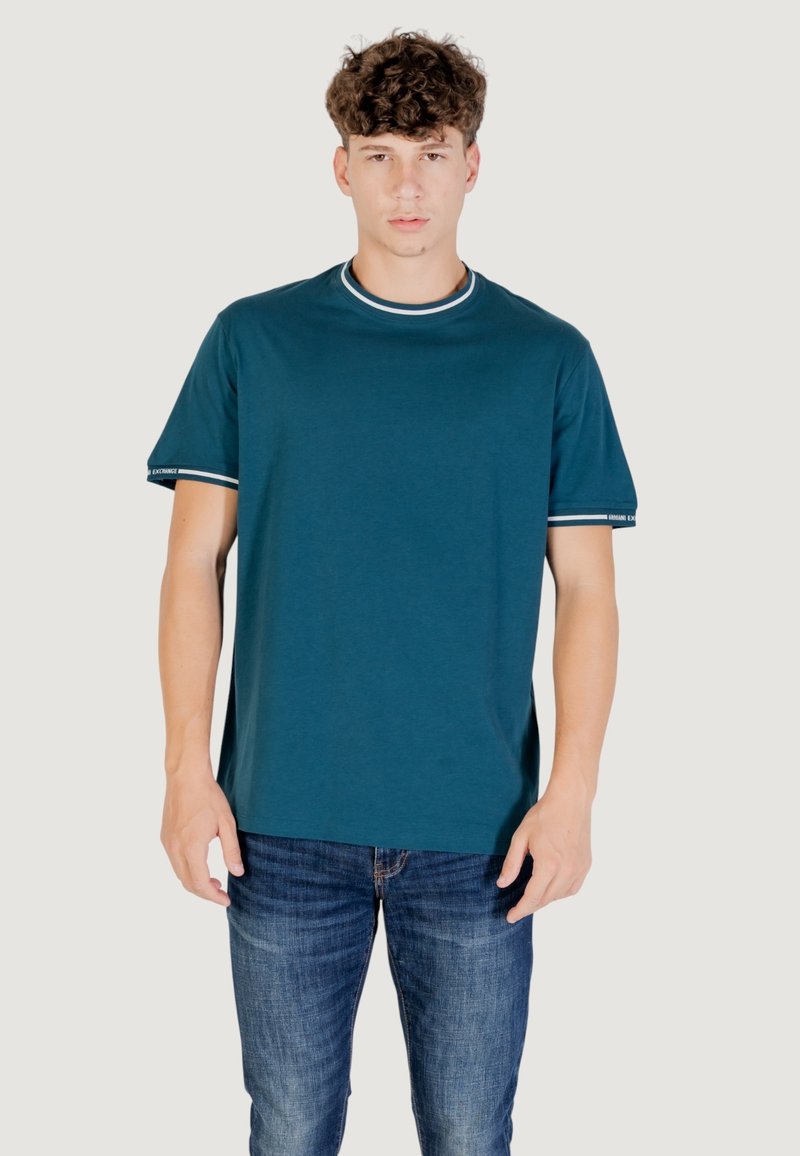 T-shirt di cotone teal con maniche corte, scollatura e strisce sulle maniche bianche a contrasto, abbinata a jeans in denim blu.