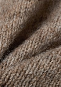 Brązowa dzianina z miękką, teksturowaną powierzchnią. Widoczne szwy tworzą ciepły, przytulny wygląd. Włókna są luźno tkane, co zwiększa miękkość.