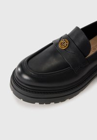 Black leather loafer with thick sole, stitched upper, and gold decorative button with bee design on strap.