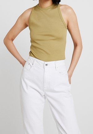 Oliwkowa zielona bluzka bez rękawów z wysokim dekoltem, w połączeniu z białymi wysokim stanem dżinsami. Materiał wydaje się miękki i dopasowany.