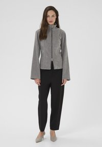 Grå, zip-up jakke med høj krave, udvidede ærmer og tekstureret stof, parret med sorte bukser og lysegrå hæle.