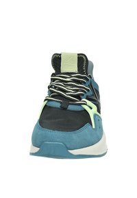 Baskets de sport présentant un mélange de daim bleu et de maille noire, des lacets texturés, des accents verts et une semelle en caoutchouc. La vue de face montre une languette rembourrée.