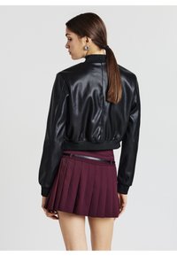 Giubbotto bomber in pelle nera con orlo a coste, maniche lunghe e un design posteriore elegante, abbinato a una gonna plissettata color bordeaux.
