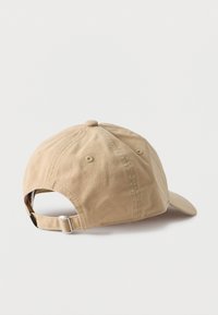 Casquette de baseball en coton beige vue de dos, avec une sangle réglable munie d'une boucle en métal, sur un fond blanc uni.