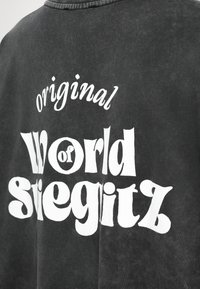 Mustvalge t-särk, millel on suured valged retrostiilis tähed, mis räägivad "originaalne World of siegitz" selja peal.