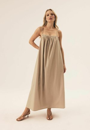 Beiges Maxi-Kleid mit verstellbaren Spaghetti-Trägern, gerafftem Ausschnitt und fließender Silhouette. Kombiniert mit braunen Blockabsatzsandalen.