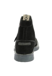 Botín de ante negro con acabado texturizado, detalles de costura blanca y suela de goma gris en contraste. Etiqueta de Kickers en el talón.