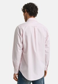 Ljusrosa långärmad skjorta med button-down krage, rundad nederkant och en mittbakfäll; tillverkad av mjukt bomullsmaterial.