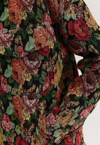 Kurtka w kwiatowy wzór z żywymi różami w kolorze czerwonym, pomarańczowym i zielonym na czarnym tle; teksturowany materiał z detalem guzikowym.