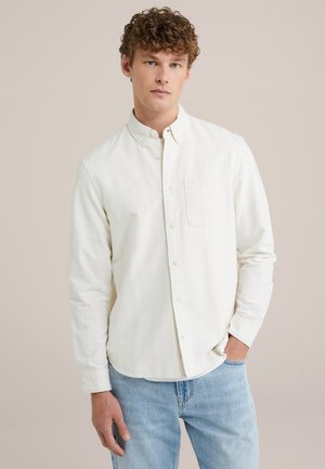Camisa de botones de manga larga, de color claro y a rayas, con un bolsillo en el pecho, hecha de tejido texturizado. Combinada con jeans de mezclilla azules.