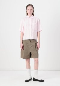 Cămașă din in roz cu mânecă scurtă și guler, asortată cu pantaloni scurți verzi măslinii, șosete albe și balerini negri. Design simplu, fără modele.