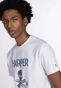 Camiseta de algodón blanca con un estampado gráfico que incluye el texto "HARPER" y un diseño de calavera, de manga corta y con un pequeño detalle en la manga.