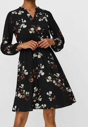 Vestido negro de manga larga, con un patrón floral en blanco y marrón. La tela es ligera, con un corte acampanado y detalles de botones.