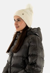 Beanie di maglia crema con pompon, caratterizzato da delicati accenti luccicanti. Giacca imbottita nera e calda con cappuccio e zip.
