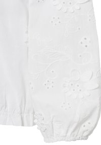Weißes Baumwollblus mit puffärmel. Verziert mit floralem Stickerei und Augenlöchern. Gekräuselte Manschetten erzeugen eine weiche Textur.