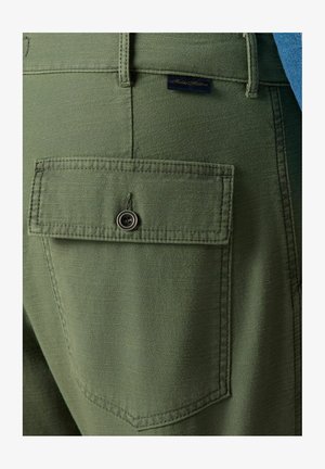 Zielone spodnie z tylną kieszenią zapinaną na guzik oraz przeszyciami. Materiał ma gładką teksturę i delikatny połysk.