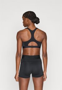 Μαύρο αθλητικό σουτιέν με σχεδιασμό racerback και λεπτομέρεια με άνοιγμα, σε συνδυασμό με εφαρμοστά μαύρα σορτς με ελαστική μέση.