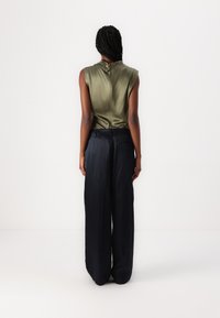 Haut sans manches en satin vert olive avec un décolleté drapé, associé à un pantalon noir à taille haute et jambes larges en tissu lisse et léger.