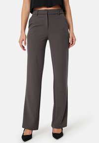 Pantalons gris taillés avec une coupe droite, dotés de passants de ceinture, de poches avant et d'une texture lisse et mate. Des talons noirs complètent le look.