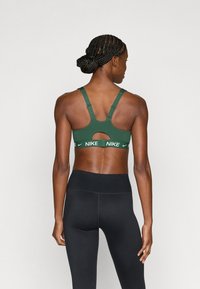 Πράσινο αθλητικό σουτιέν με κοψίματα και ρυθμιζόμενους ιμάντες. Διαθέτει λουρί με λευκές επιστρώσεις με λογότυπο. Συνδυάζεται με μαύρο κολάν.