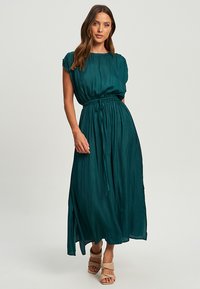 Teal, flowing maxi dress in lightweight fabric with short sleeves and an elastic waist. Features a gathered, relaxed fit with side slits.