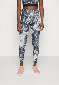 Legginsy w kwiatowy wzór w granatowo-białe barwy, wykonane z elastycznego materiału. Połączone z czarnym topem typu crop i jasnoróżowymi butami sportowymi.