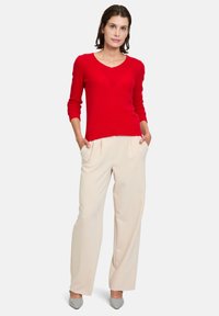 Pull rouge en tricot avec un col en V et des manches longues, associé à un pantalon taille haute beige et des chaussures à talons carrés grises.