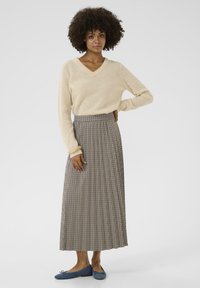 Beiger Strick-V-Ausschnitt-Pullover, langer karierter Rock in Braun und Creme sowie blaue Ballerinas. Fokus auf Textur, Muster und entspannte Passform.