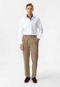 Witte button-up shirt met een bruine patroon kraag, gecombineerd met lichtbruine geplooide broek en donkere schoenen. Soepele textuur, op maat gemaakte pasvorm.