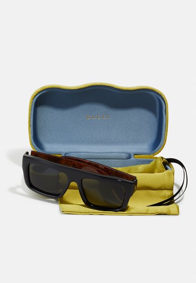 Occhiali da sole Gucci con montatura quadrata nera e lenti scure, inseriti in una custodia blu e gialla, dotata di un morbido sacchetto in microfibra giallo.
