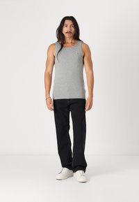 Tricou gri din bumbac cu guler rotund, asortat cu blugi negri și adidași albi, prezentat pe un model masculin cu păr lung.