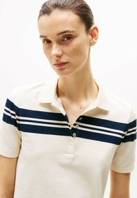 Polo shirt i creme med marineblå striber, med en krave og tre knapper. Stoffet ser glat ud med et struktureret design.