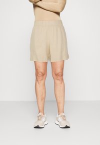 Shorts beige clair en tissu doux avec une taille élastique, présentant une coupe droite et des poches latérales. Portés avec des chaussures de sport beige.